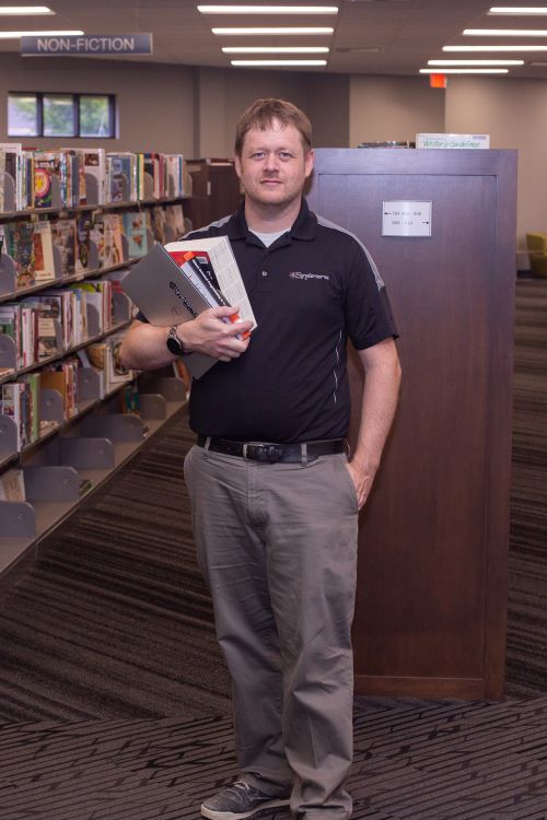 entrepreneur standing in library holding books and computer