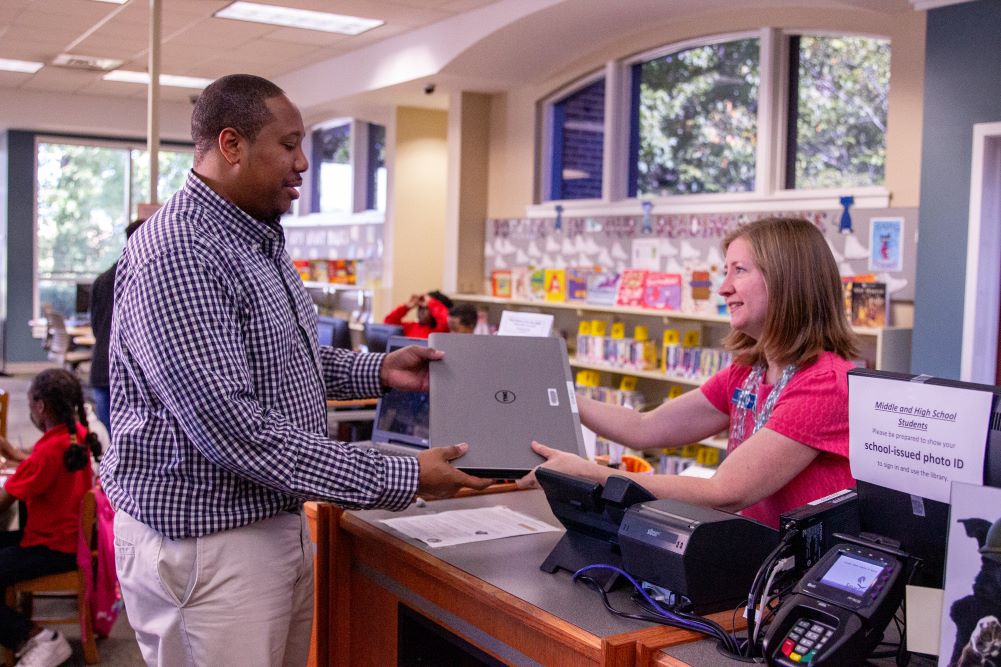woman handing man a laptop inside a library