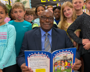 man holding and reading a book to young elementary school students