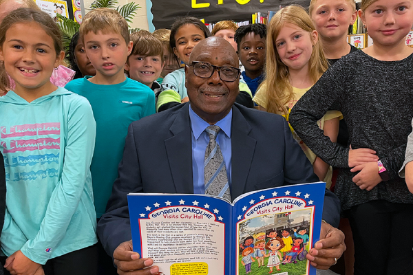 man holding and reading a book to young elementary school students